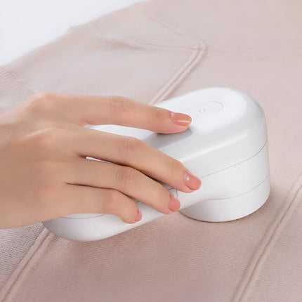 A close-up of a hand using a small white handheld fabric shaver on a light beige garment.  peetta-best online store uae