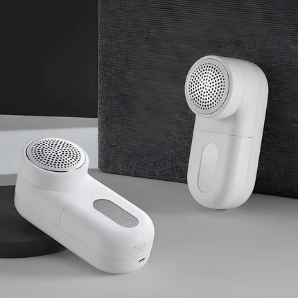 Two white handheld lint remover devices shown on a clean studio surface, one resting on a black base and one standing upright against a dark textured backdrop.peetta-Lint_Remover_Efficient_Fabric_Shaver_and_Lint_Roller_for_Clothes_and_Upholstery-best_online_store_uae_4