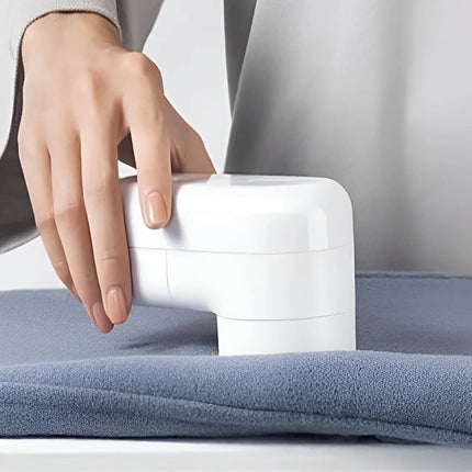 A close-up of a person's hand using a white handheld fabric shaver on a blue-gray fleece blanket. peetta-Lint_Remover_Efficient_Fabric_Shaver_and_Lint_Roller_for_Clothes_and_Upholstery-best_online_store_uae_4
