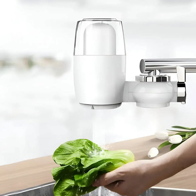 A white and chrome kitchen faucet filter attachment mounted on a faucet above a sink, with water running while a hand washes green lettuce. A human hand is visible, so this is classified as Lifestyle. .peetta-best online uae store