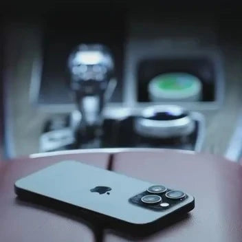A silver Apple iPhone with a dark case is shown from the back, resting on a brown leather surface with a blurred car interior in the background. peetta-VacuumSuctionCarMount-MagneticUniversalPhoneHolder1